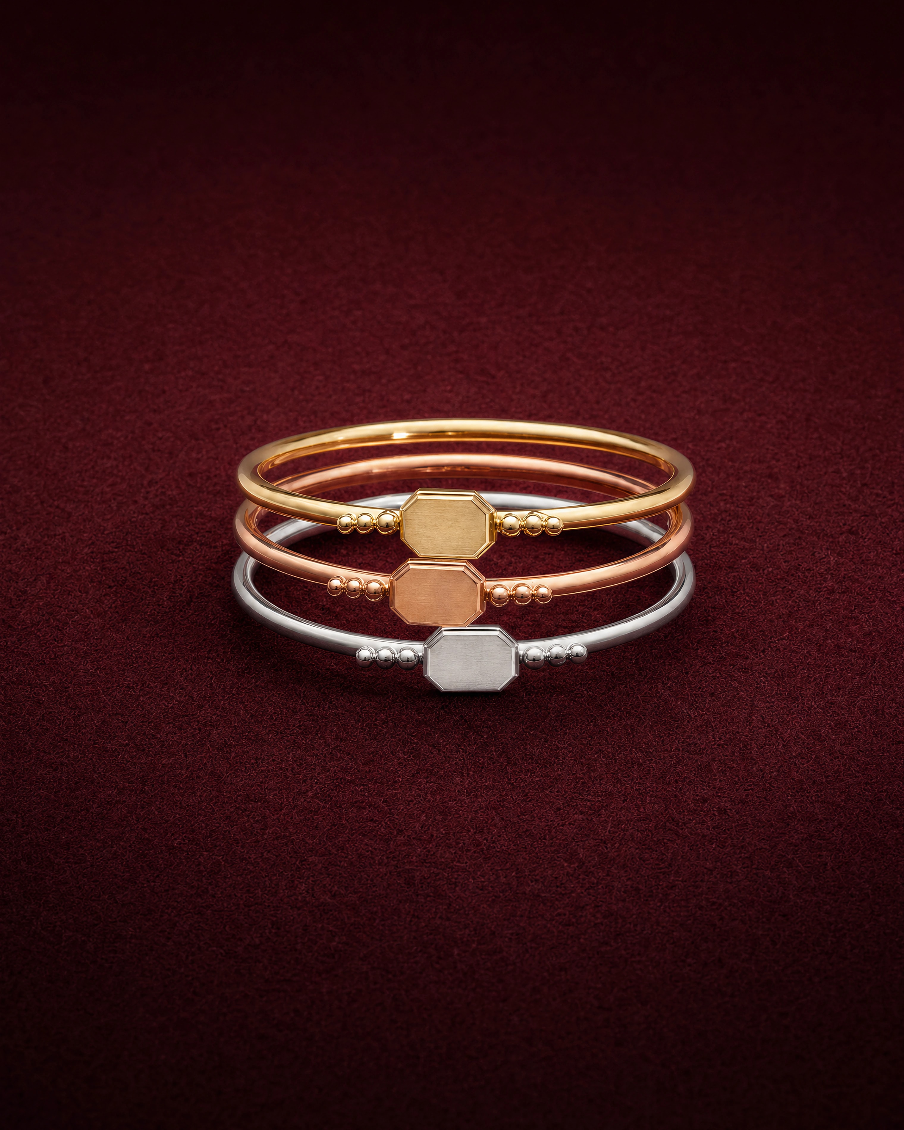 Three Thread Stacking Rings in yellow, rose and white gold, each with a small octagonal plate, on garnet jeweler's felt